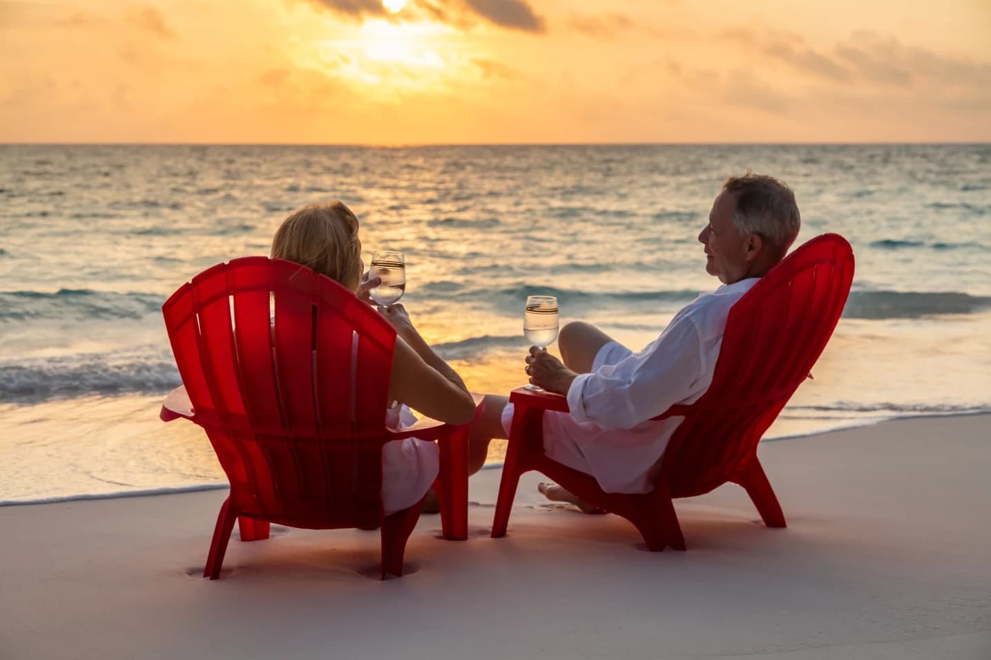 senior-couple-sitting-on-a-beach-at-sunset-smiling-and-planning-their-retirement-activities